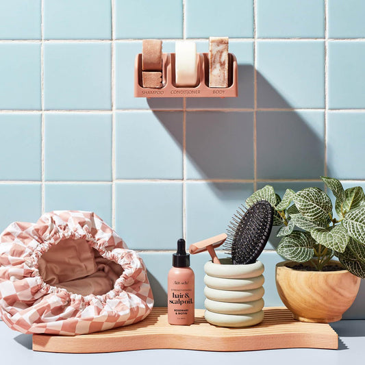 Bathroom setting with hair care products, a pink shower cap, and a plant on a blue tiled wall background.
