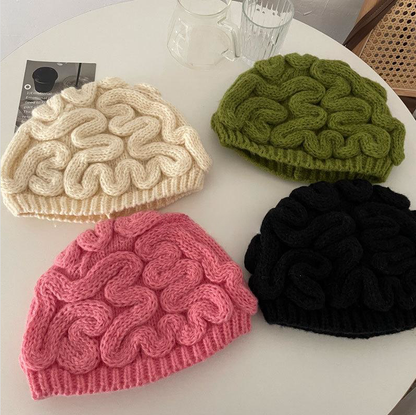 Four knitted brain-pattern hats in beige, green, pink, and black on a white surface.