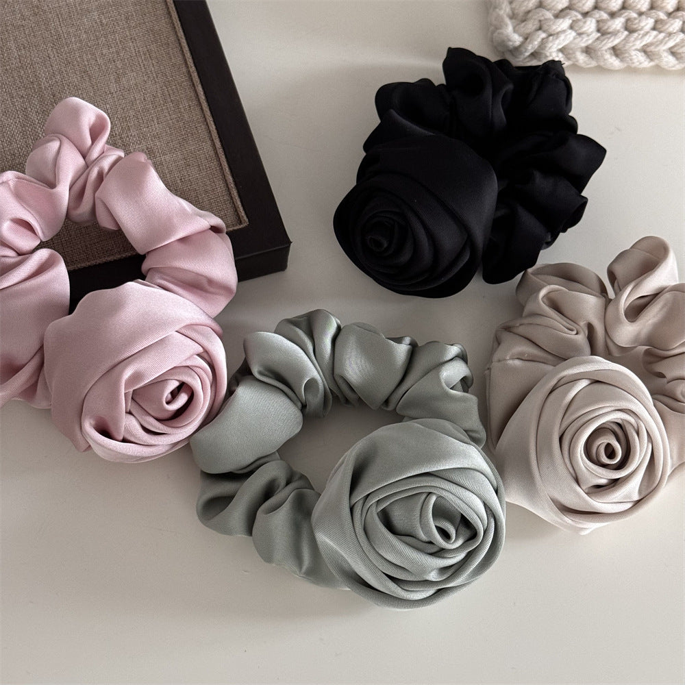 Set of three fabric scrunchies in pink, black, and gray on a light surface.