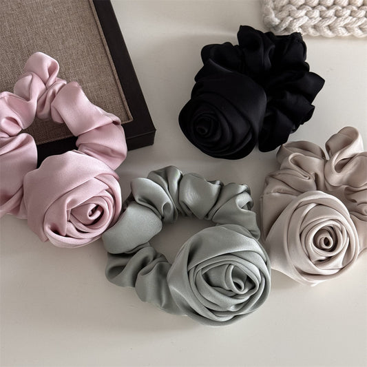 Set of three fabric scrunchies in pink, black, and gray on a light surface.