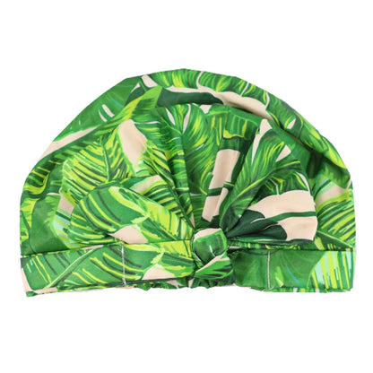 A green tropical leaf print turban cap with a knotted front detail, shown against a plain white background.