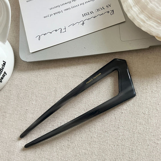 Black hairpin on a textured surface with a card and envelope in the background